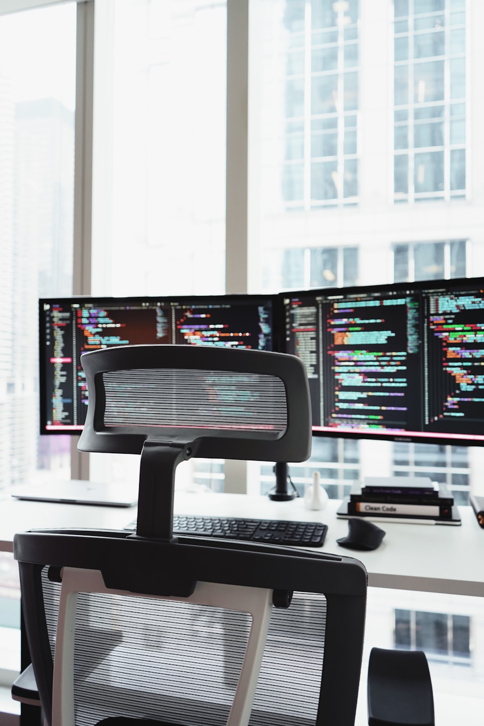 Two computer monitors showing code on a white desk.